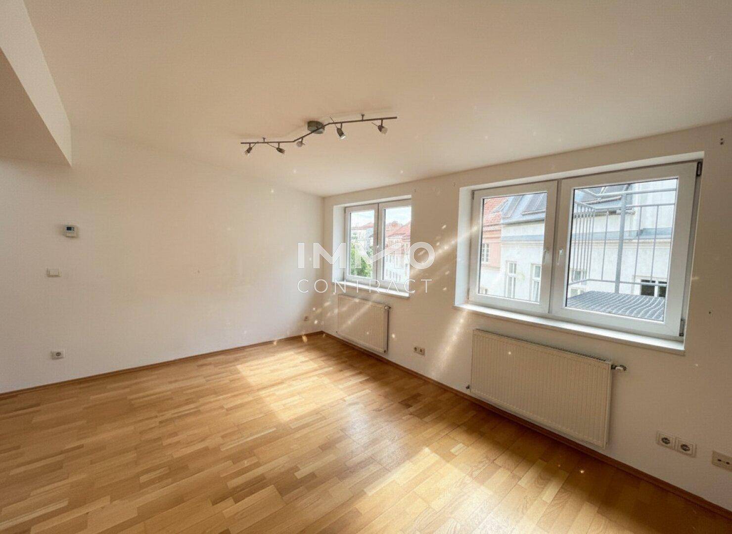 Lichtdurchfluteter Raum mit Parkettboden und zwei großen Fenstern, ideal als Wohn- oder Schlafzimmer.