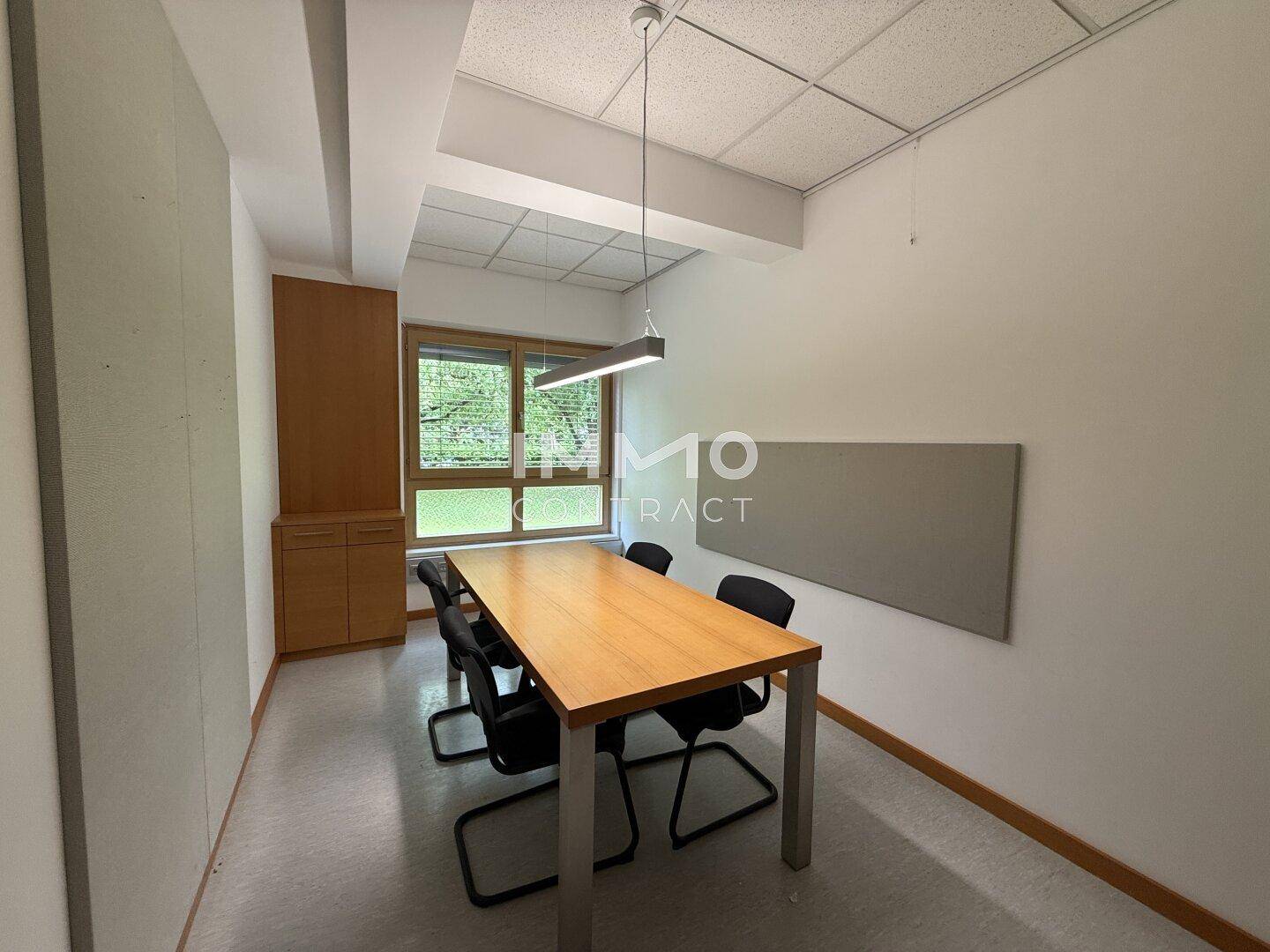 Konferenzraum mit Holztisch, Stühlen und einer großen Wandtafel.