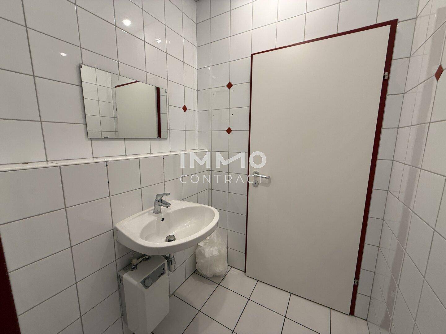 Kleine Toilette mit Waschbecken, Spiegel und weißen Fliesen an den Wänden.