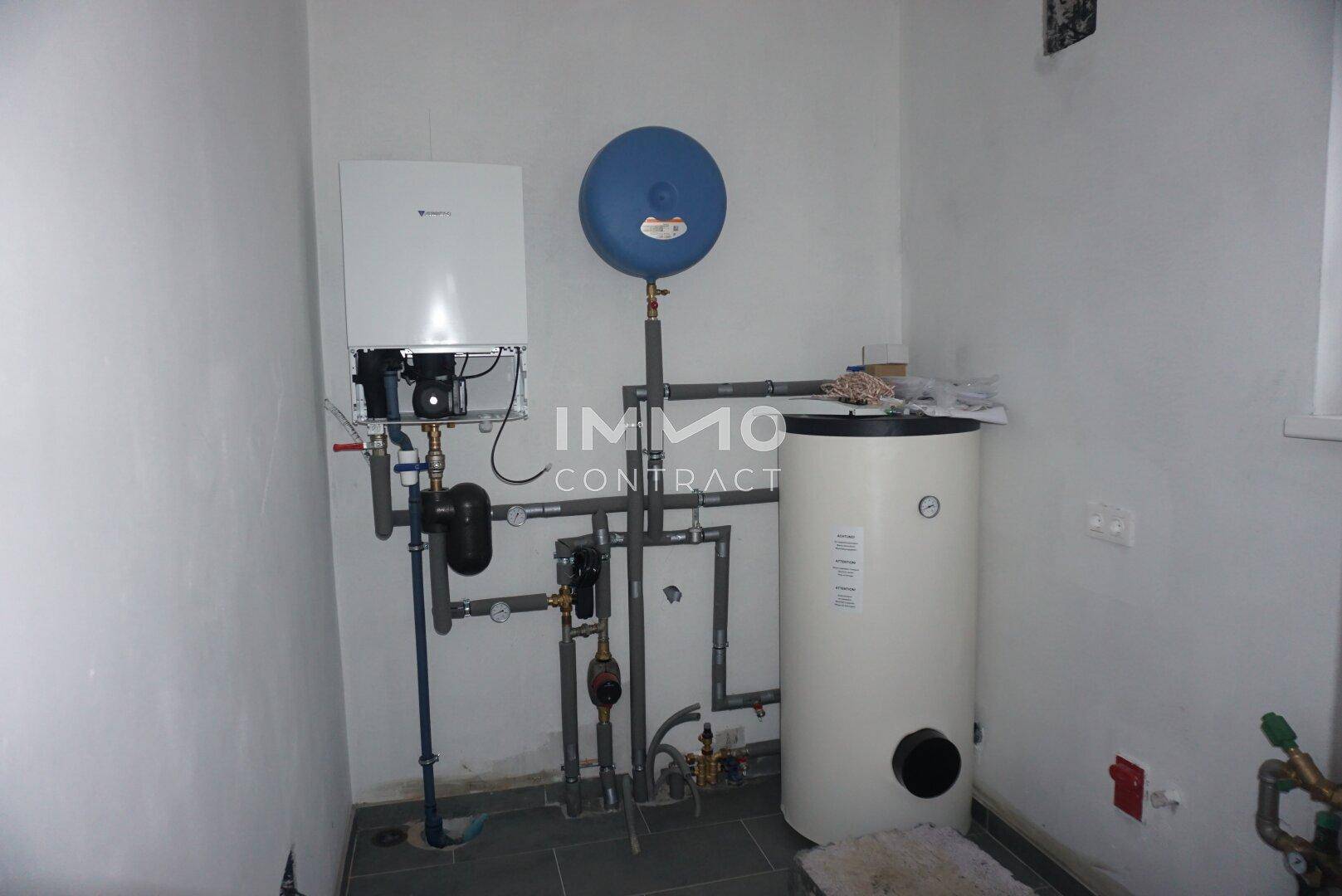 Hauswirtschaftsraum mit Heizungsanlage, Warmwasserspeicher und sichtbaren Installationen an der Wand.