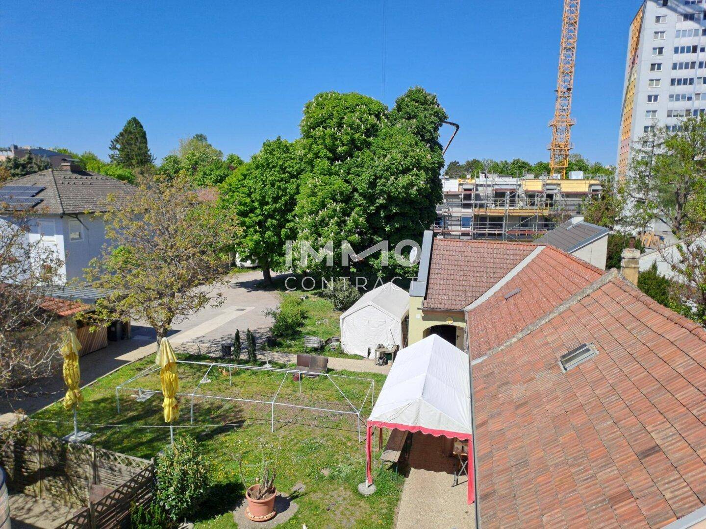 Blick von oben auf einen grünen Gartenbereich mit Bäumen, Zelten und umliegenden Gebäuden.