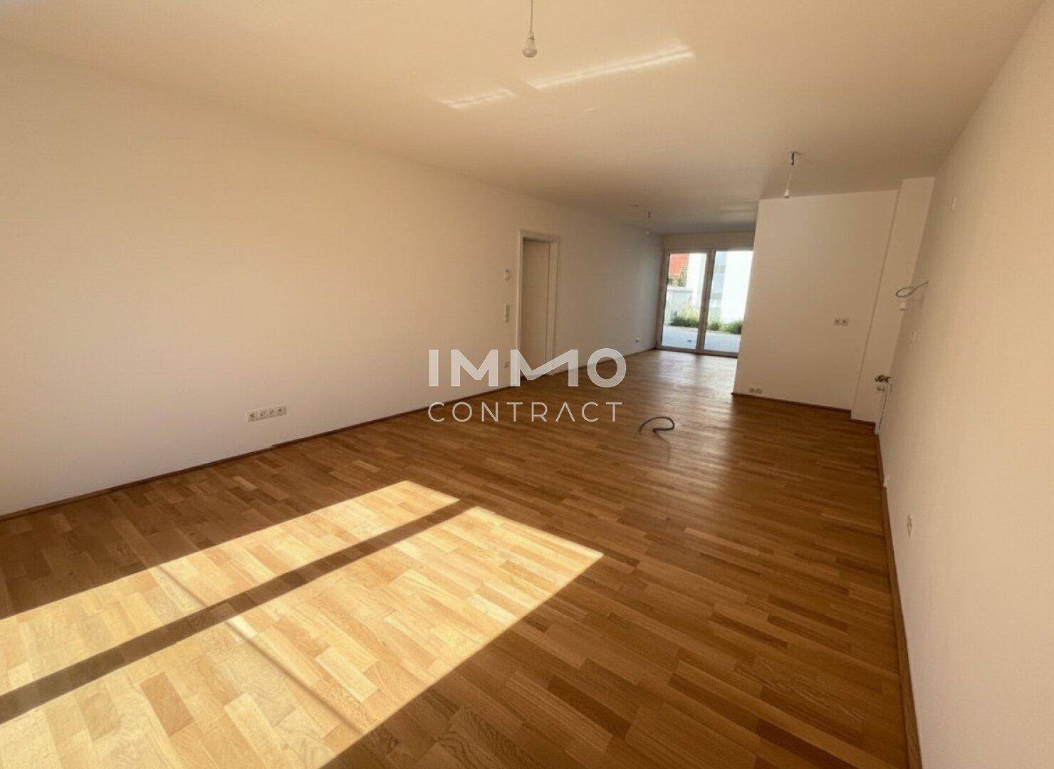 Helles Wohnzimmer mit Parkettboden und großen Fenstern, die viel Tageslicht hereinlassen.