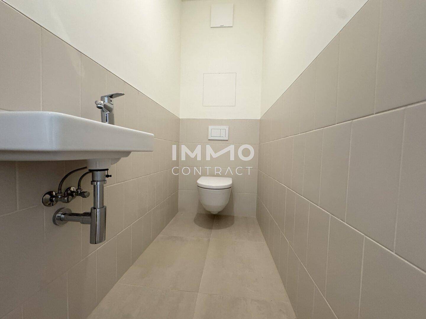 Kleines Gäste-WC mit Wand-WC, Waschbecken und hellen Fliesen.