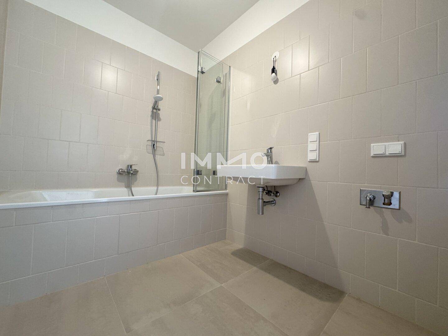 Modernes Badezimmer mit Badewanne, Duschabtrennung und hellem Fliesenboden.