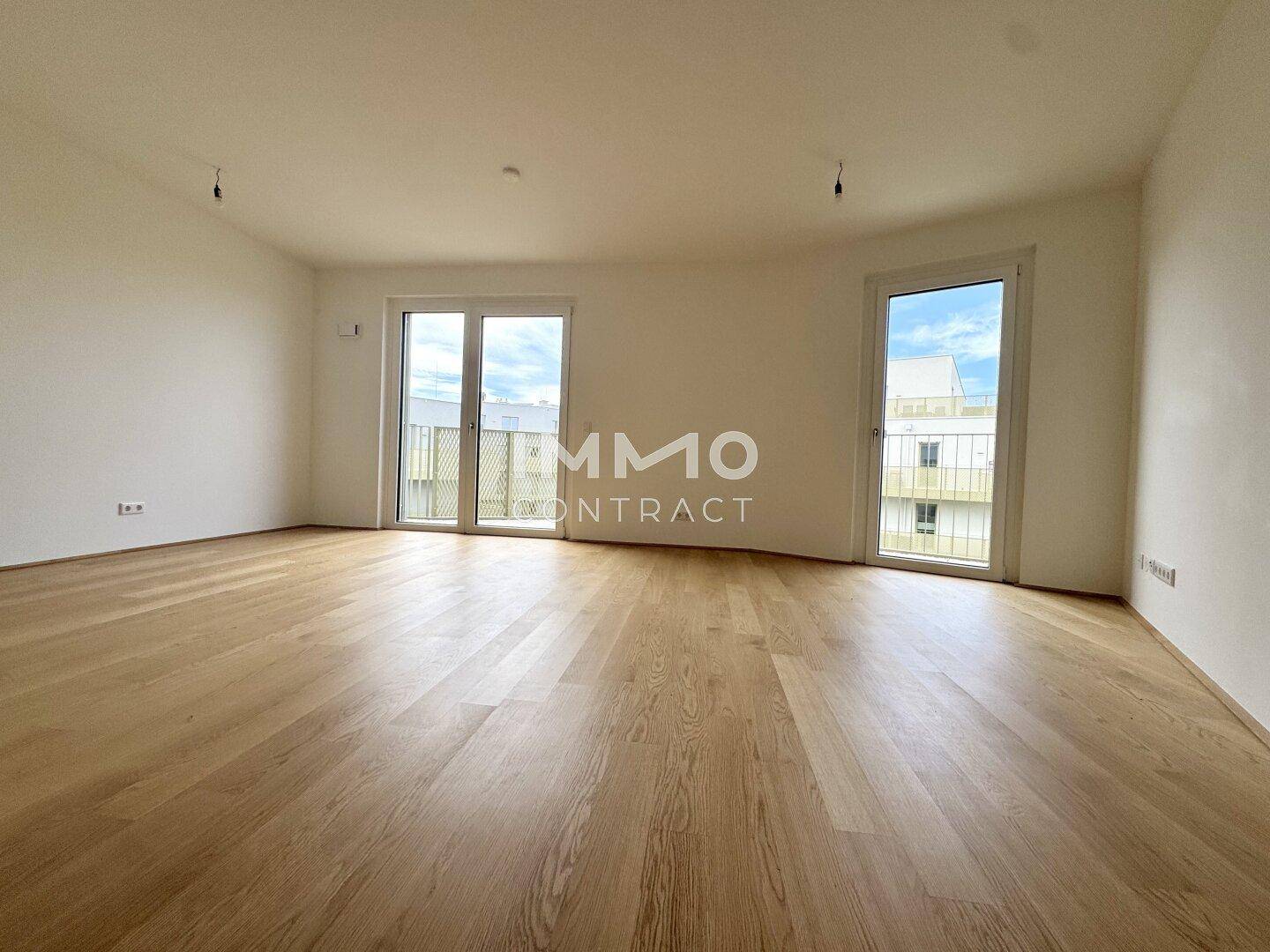 Helles, leeres Zimmer mit Holzboden und Zugang zu einem französischen Balkon.