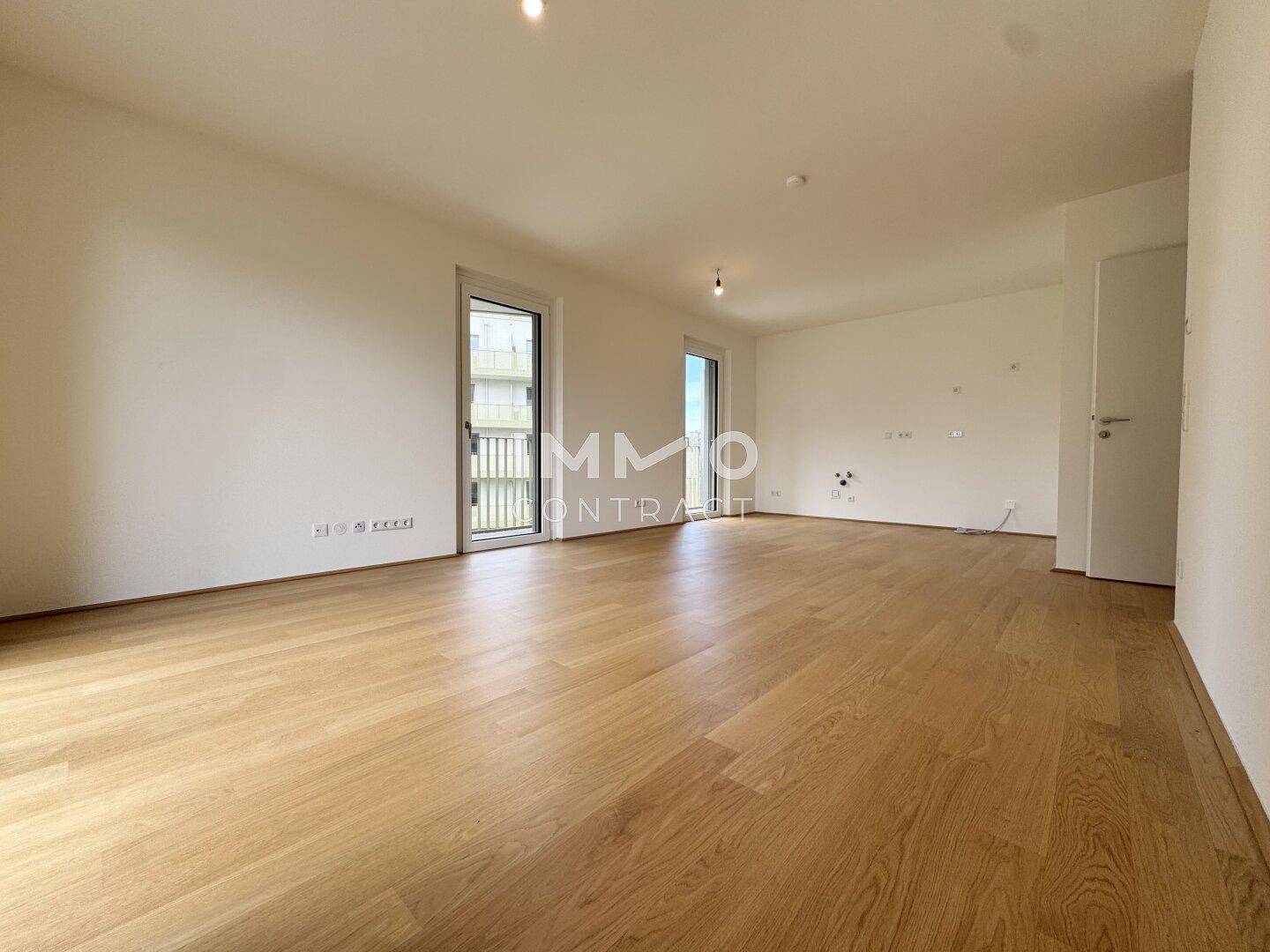 Geräumiger, leerer Raum mit hellem Holzboden und zwei Zugängen zum Balkon.