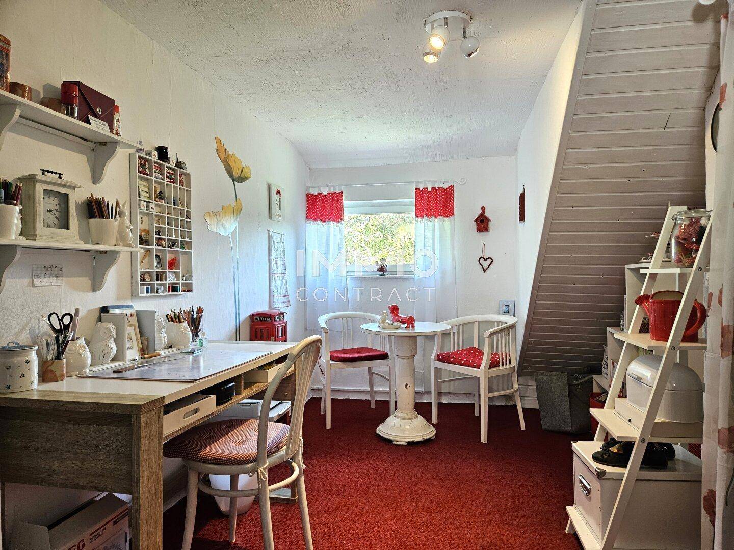 Kreativer Arbeitsbereich mit Schreibtisch, rotem Teppichboden und einem kleinen Tisch mit Stühlen.