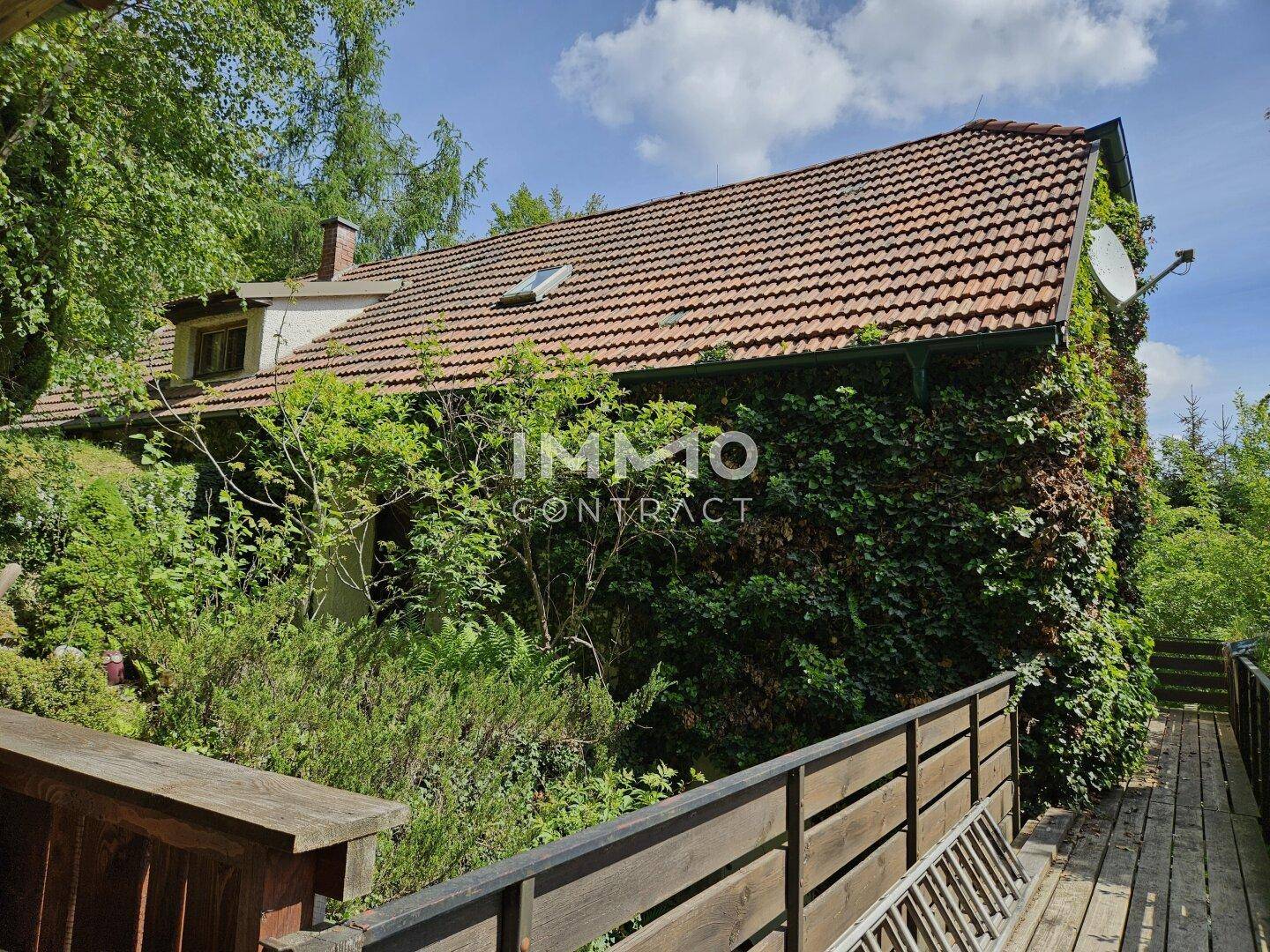 Charmantes Haus mit Ziegeldach, vollständig von Efeu bewachsen, umgeben von viel Grün.