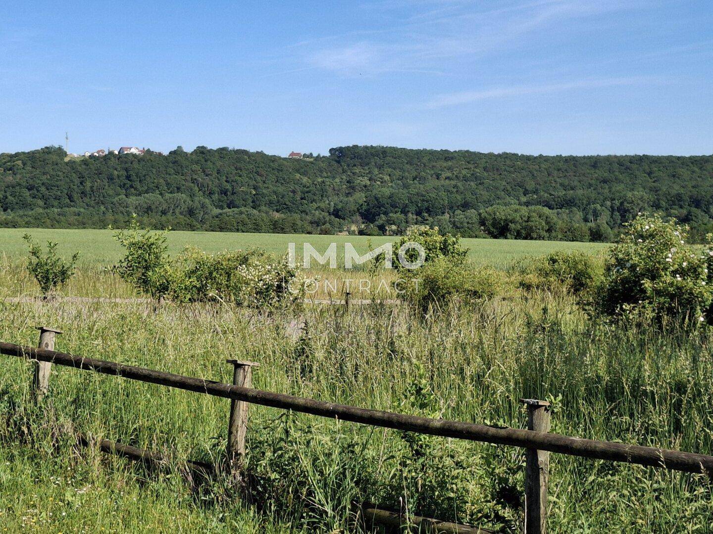 Grüne Wiesen und Felder mit einem Holzzaun im Vordergrund unter strahlend blauem Himmel.