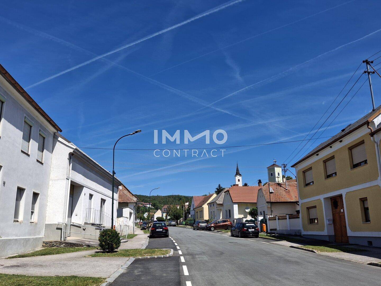 Ruhige Wohnstraße mit traditionellen Häusern und einem Kirchturm im Hintergrund.