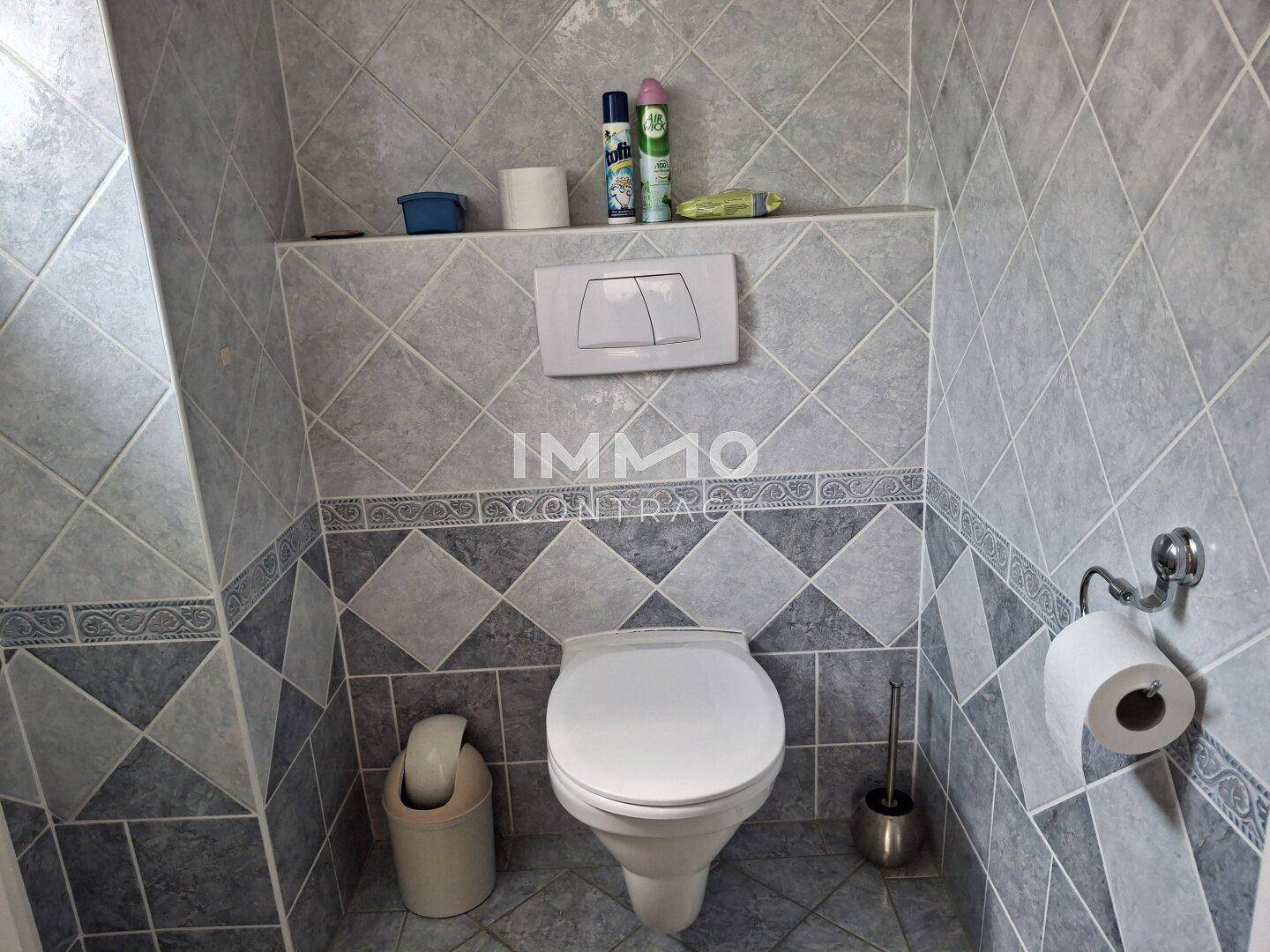 Separate Toilette mit Wand-WC und grauen Fliesen in Rautenmuster.