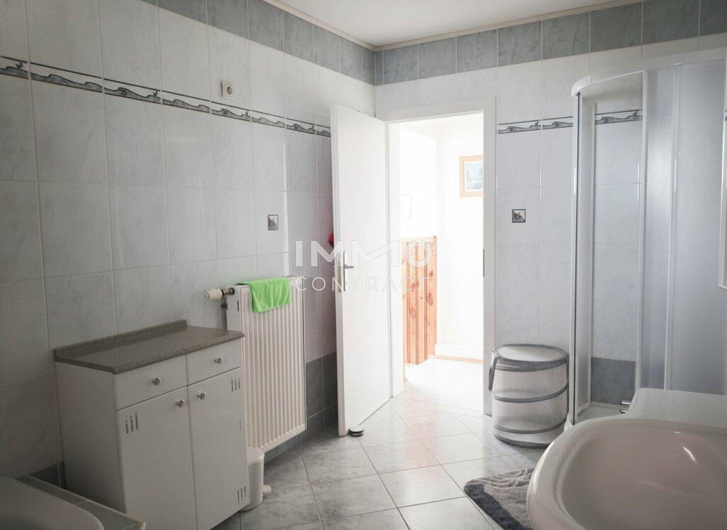Geräumiges Badezimmer mit Dusche, Waschbecken und Zugang zum Flur.