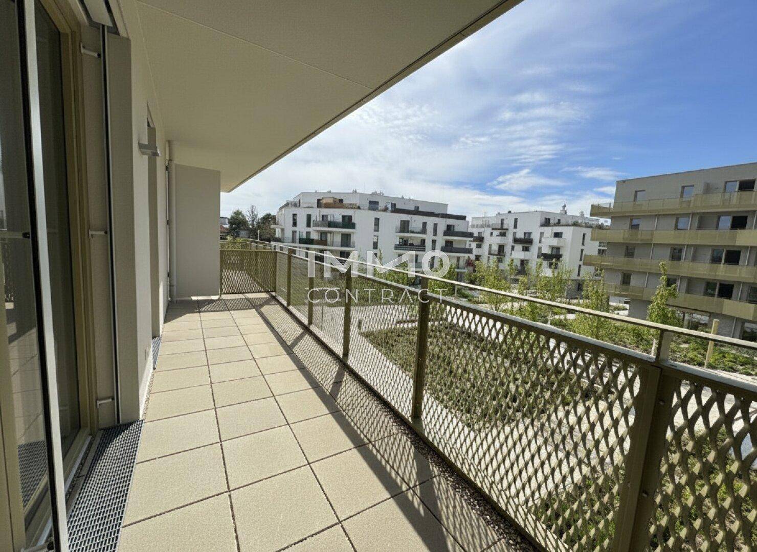 Langer Balkon mit Fliesenboden und Metallgeländer, bietet Blick auf moderne Wohngebäude und Grünflächen.