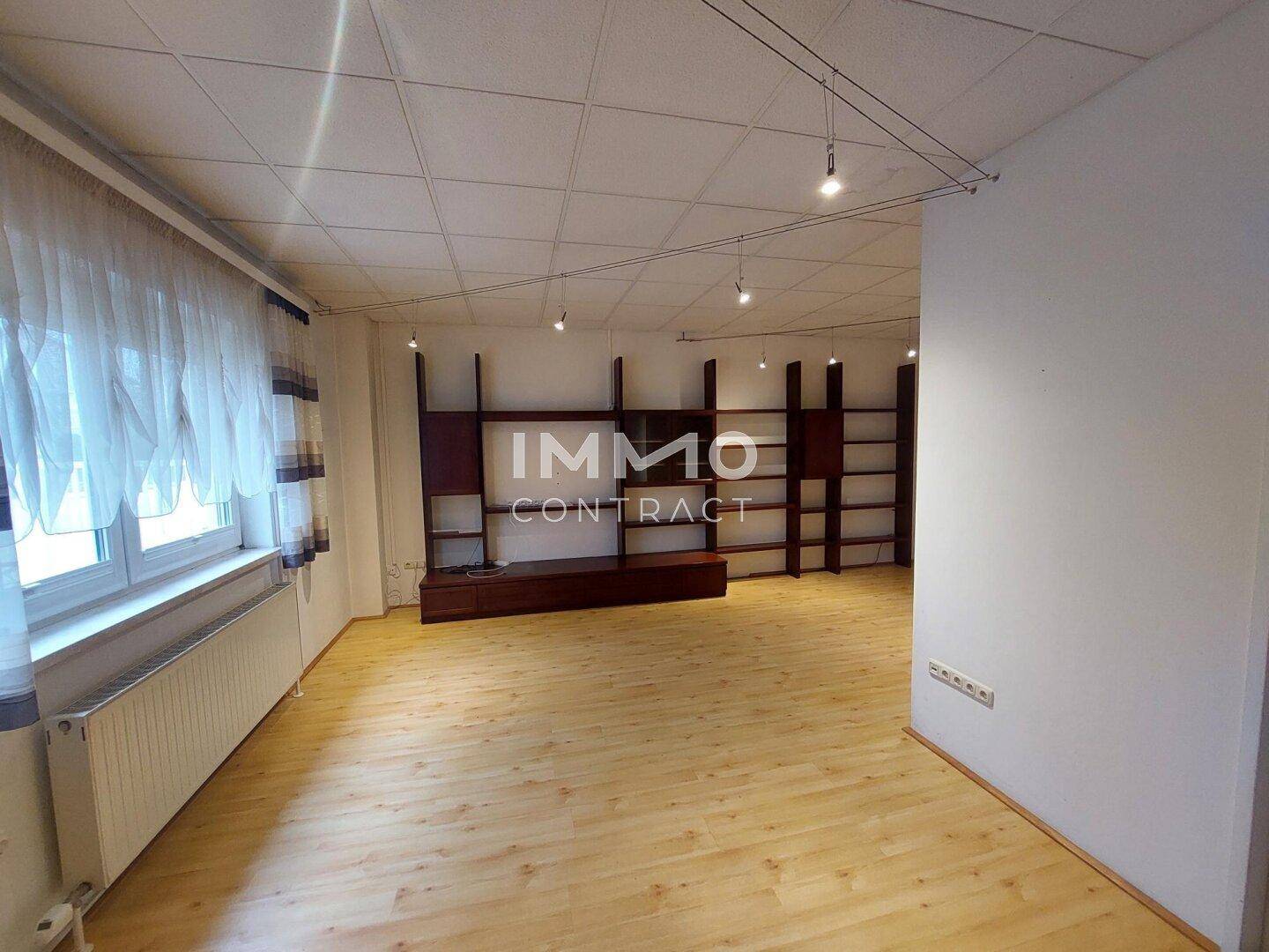 Geräumiges Wohnzimmer mit Laminatboden, Einbauregalen und Deckenstrahlern.