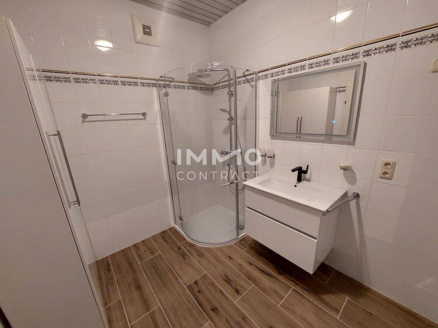 Modernes Badezimmer mit Duschkabine, Waschbecken und Fliesenboden in Holzoptik.