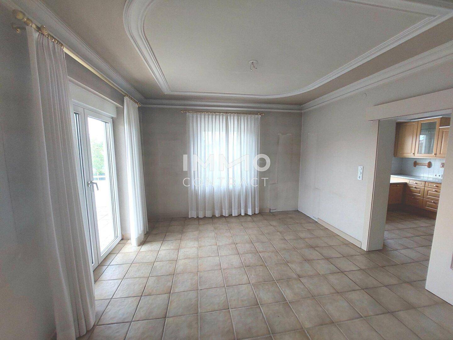Helles Wohnzimmer mit Fliesenboden, Stuckdecke und Zugang zur Terrasse.
