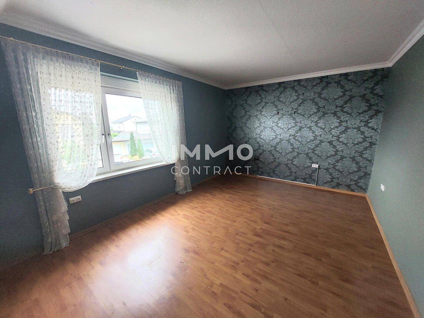 Schlafzimmer mit Laminatboden, gemusterter Tapete und großem Fenster.