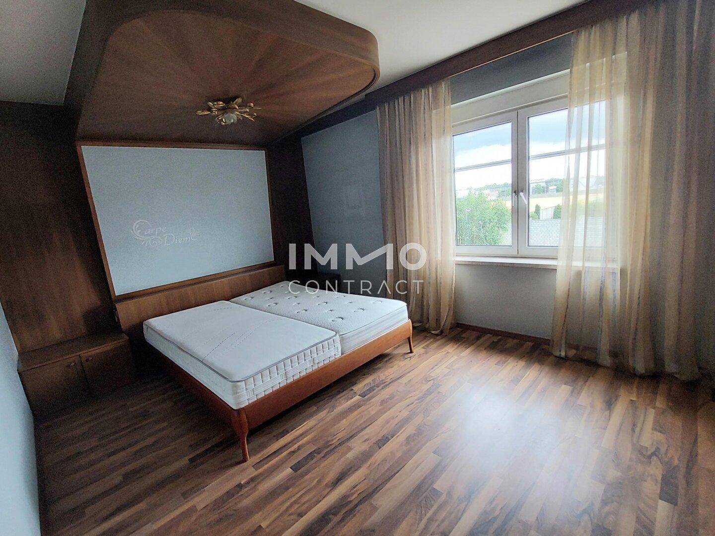 Schlafzimmer mit Holzbett, Laminatboden und großem Fenster mit Ausblick.