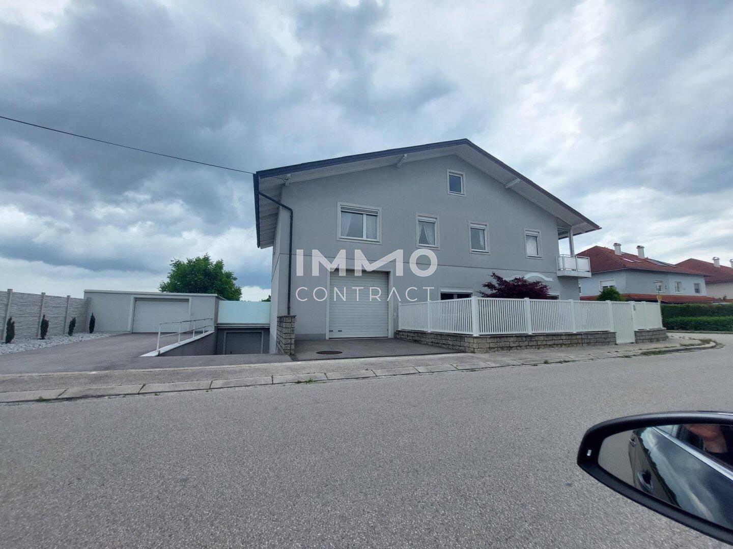 Graues Einfamilienhaus mit Garagenzufahrt und gepflegtem Vorgarten.
