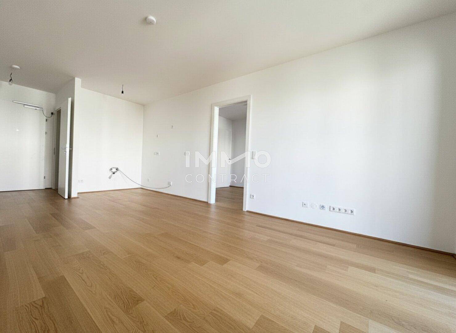 Geräumiger, heller Raum mit hochwertigem Parkettboden und mehreren Türöffnungen.