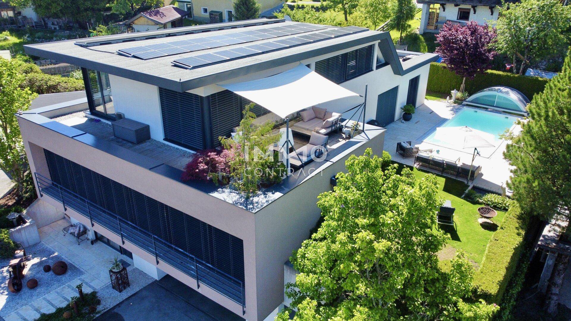 Luftaufnahme eines modernen Hauses mit Pool, Dachterrasse und Photovoltaikanlage auf dem Flachdach.