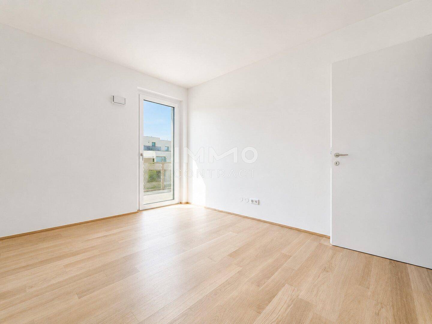 Unmöbliertes Schlafzimmer mit hellem Parkettboden und Zugang zu einem Balkon, bietet viel Tageslicht.