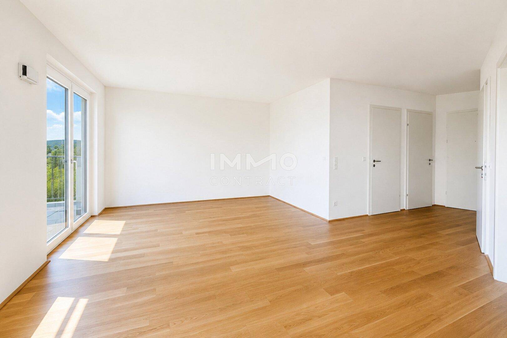 Geräumiges, helles Zimmer mit Holzboden und großen Fenstern, die viel Licht hereinlassen.