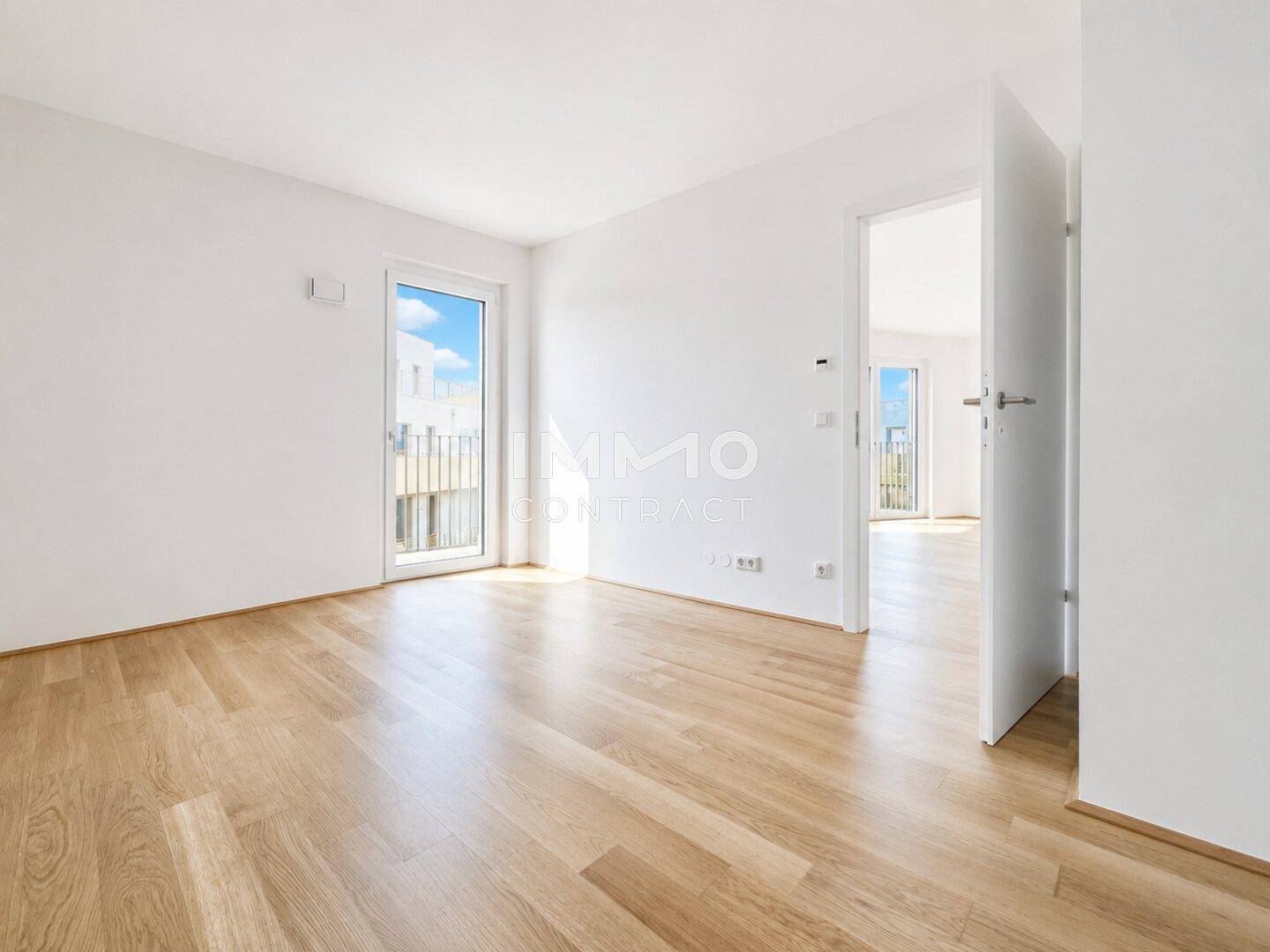 Heller Raum mit Parkettboden und Zugang zu einem Balkon, verbunden mit einem weiteren Zimmer.