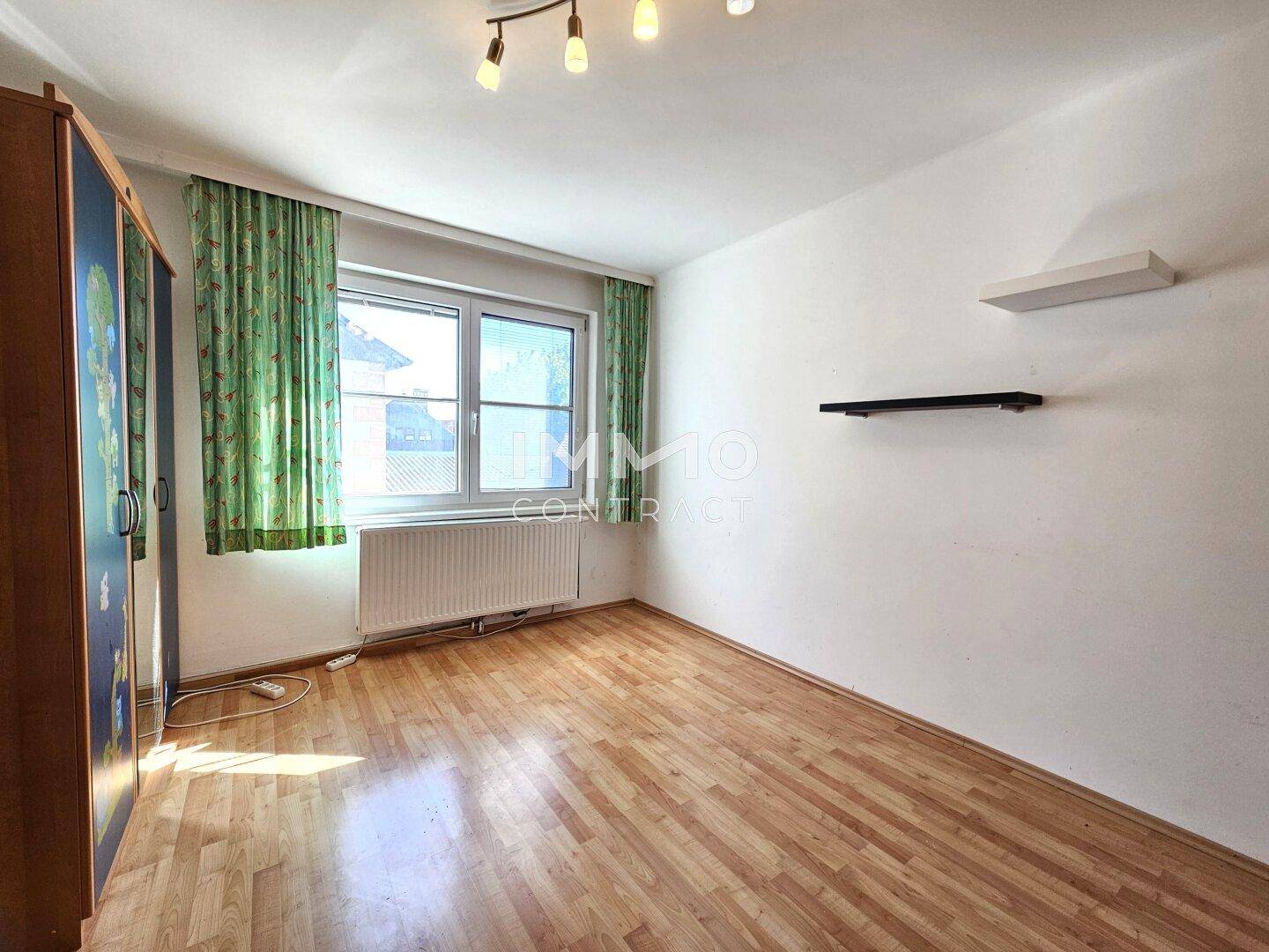 Helles Kinderzimmer mit Laminatboden, großem Fenster und Vorhängen, bietet viel Tageslicht.