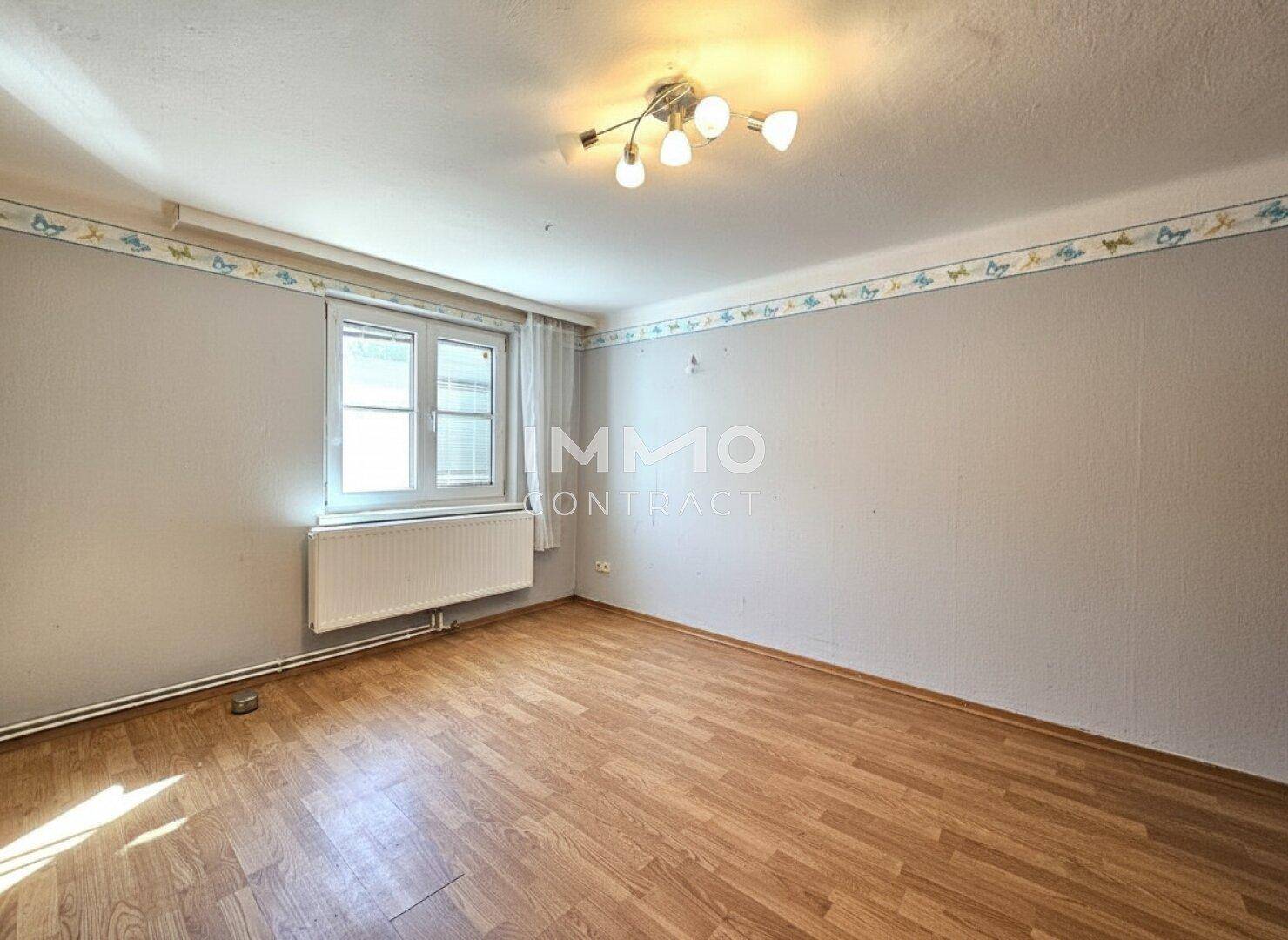 Helles Zimmer mit Laminatboden, Fenster und Heizkörper, bereit zur individuellen Gestaltung.