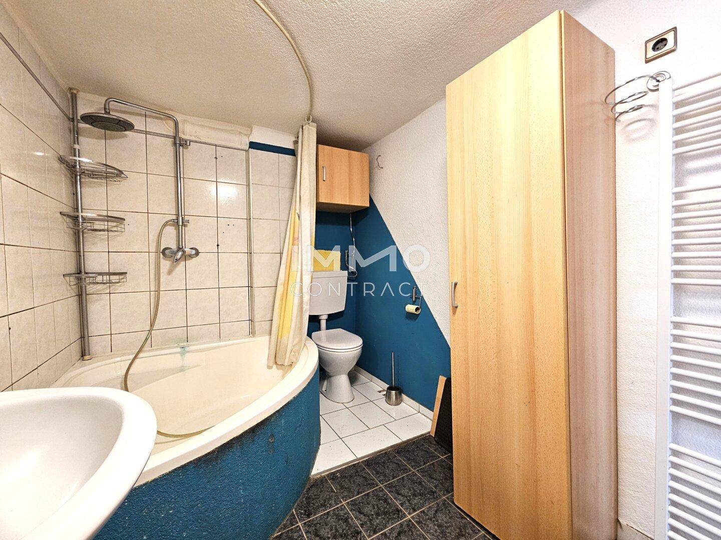 Badezimmer mit Toilette, Eckbadewanne und Heizkörper, funktional und einfach gestaltet.