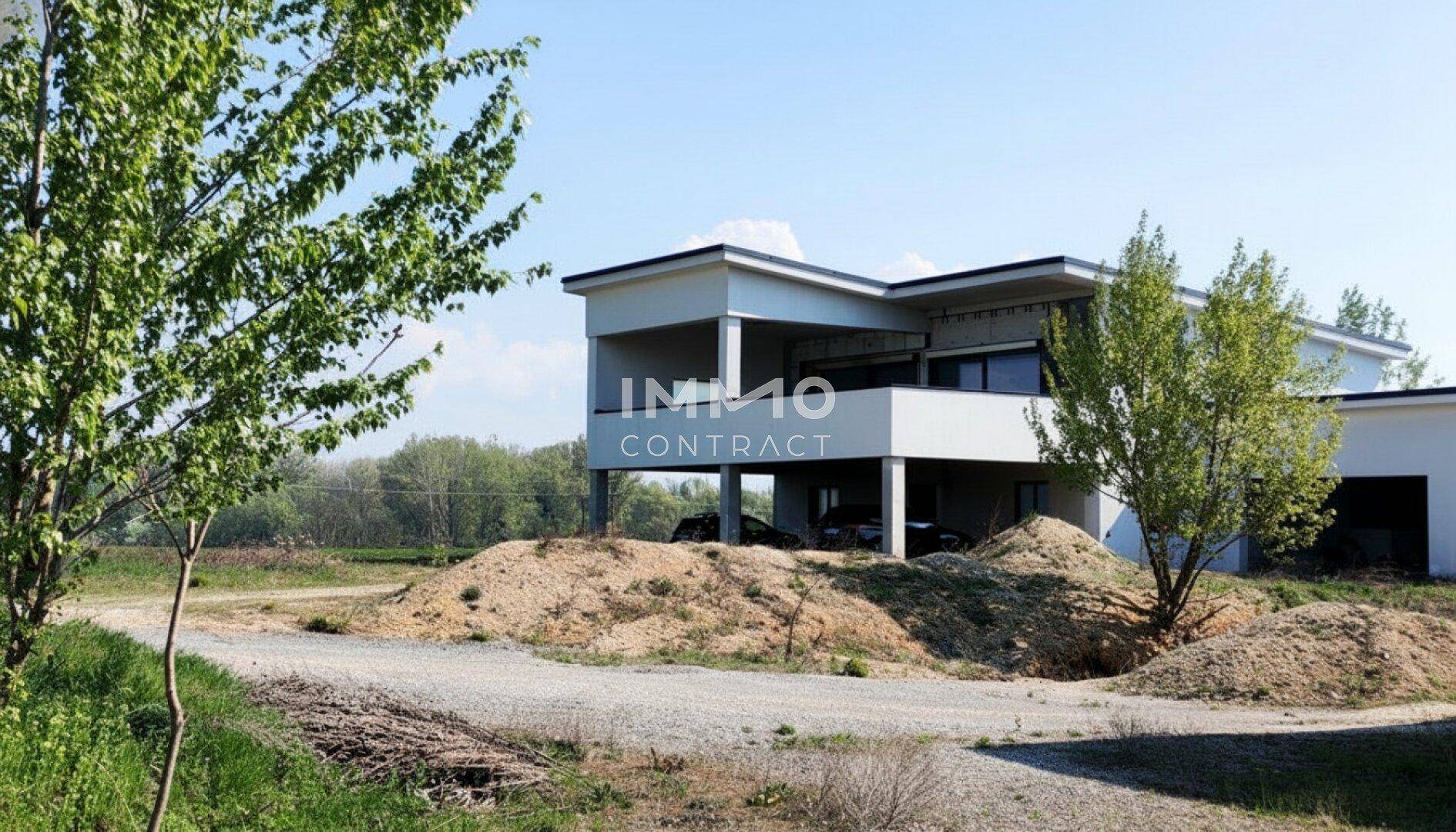 Nahaufnahme des modernen Rohbaus mit überdachtem Balkonbereich und umliegender Baustellenlandschaft.