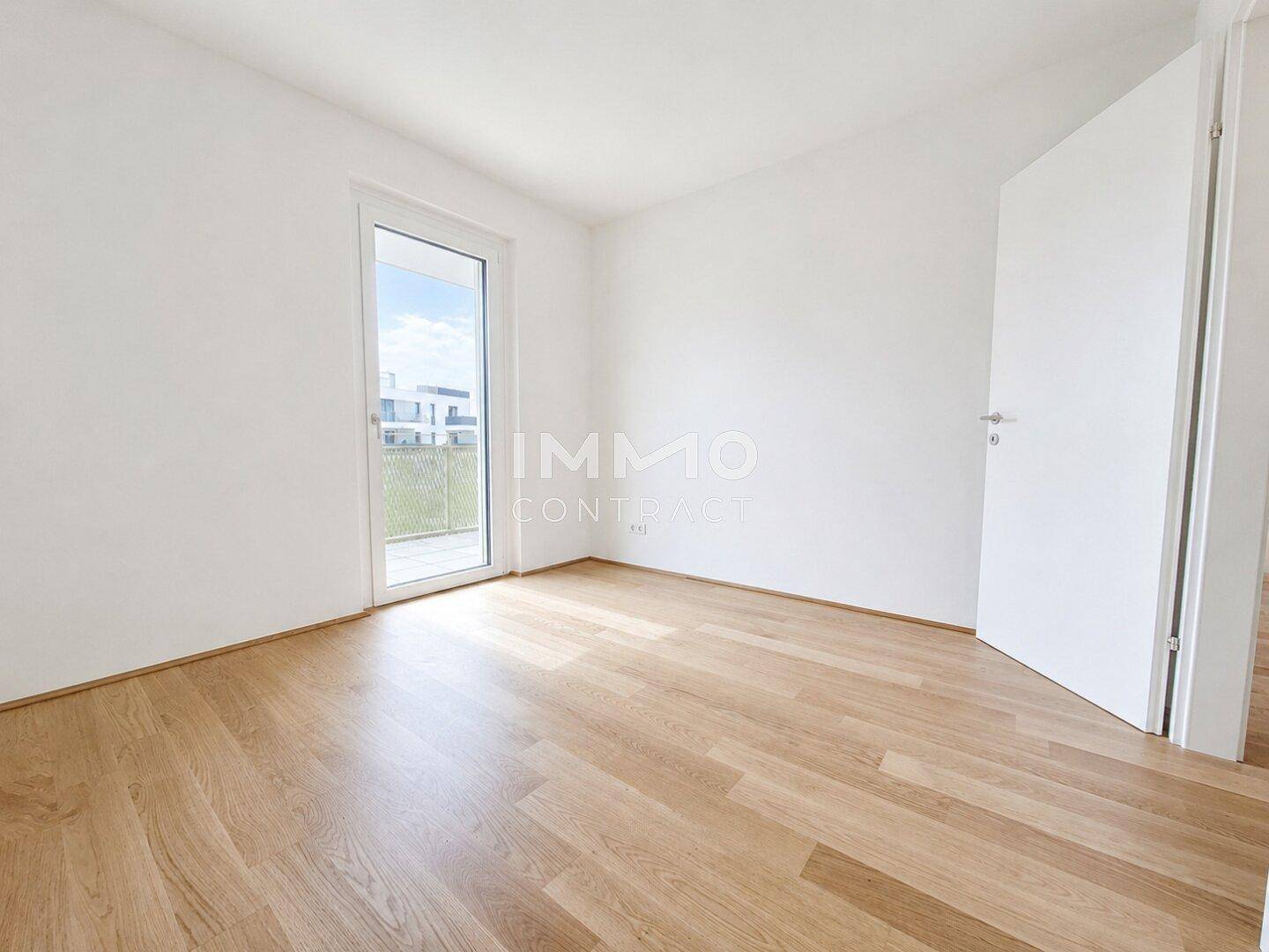 Schlafzimmer mit hellem Holzboden, weißen Wänden und direktem Balkonzugang.