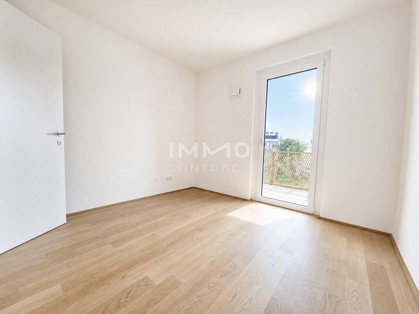 Sonniges Zimmer mit Holzboden, weißen Wänden und Zugang zu einem Außenbereich.