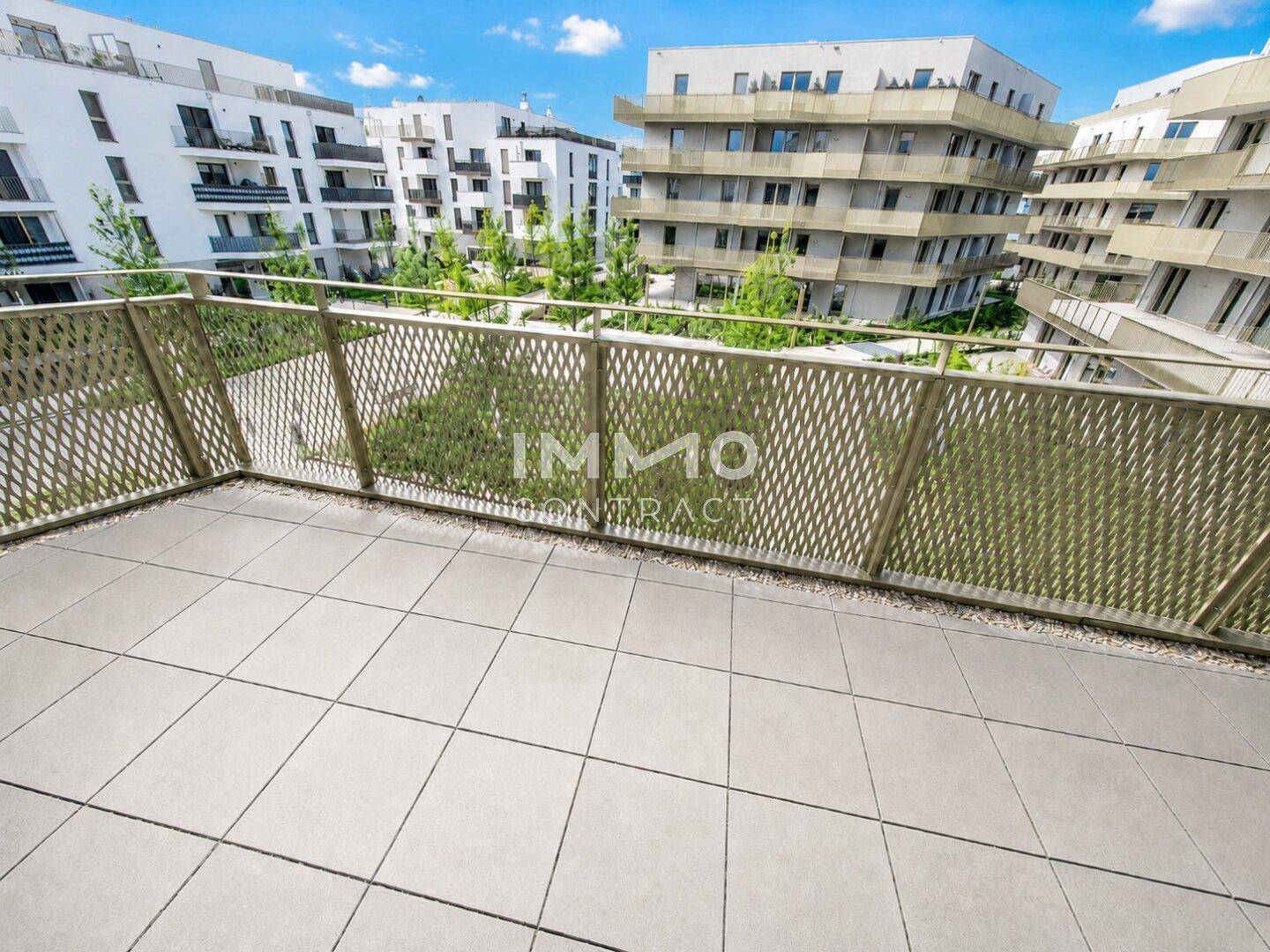 Geräumiger Balkon mit Fliesenboden und Blick auf moderne Wohngebäude und Grünflächen.