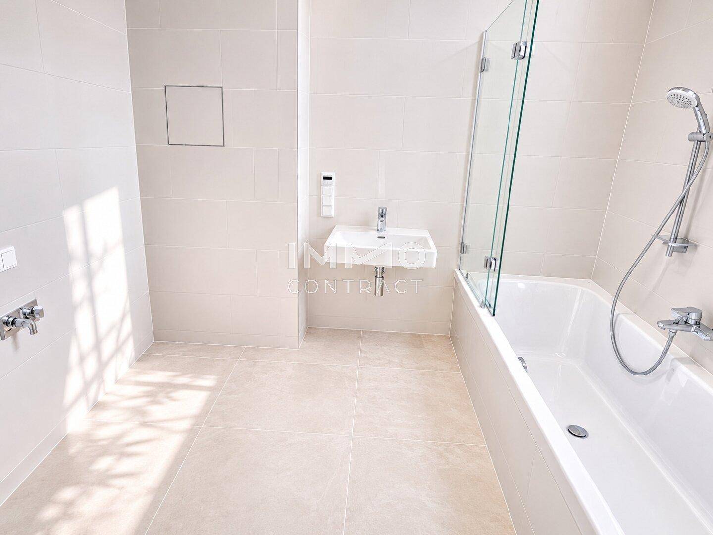 Modernes Badezimmer mit hellen Fliesen, Badewanne und wandmontiertem Waschbecken.