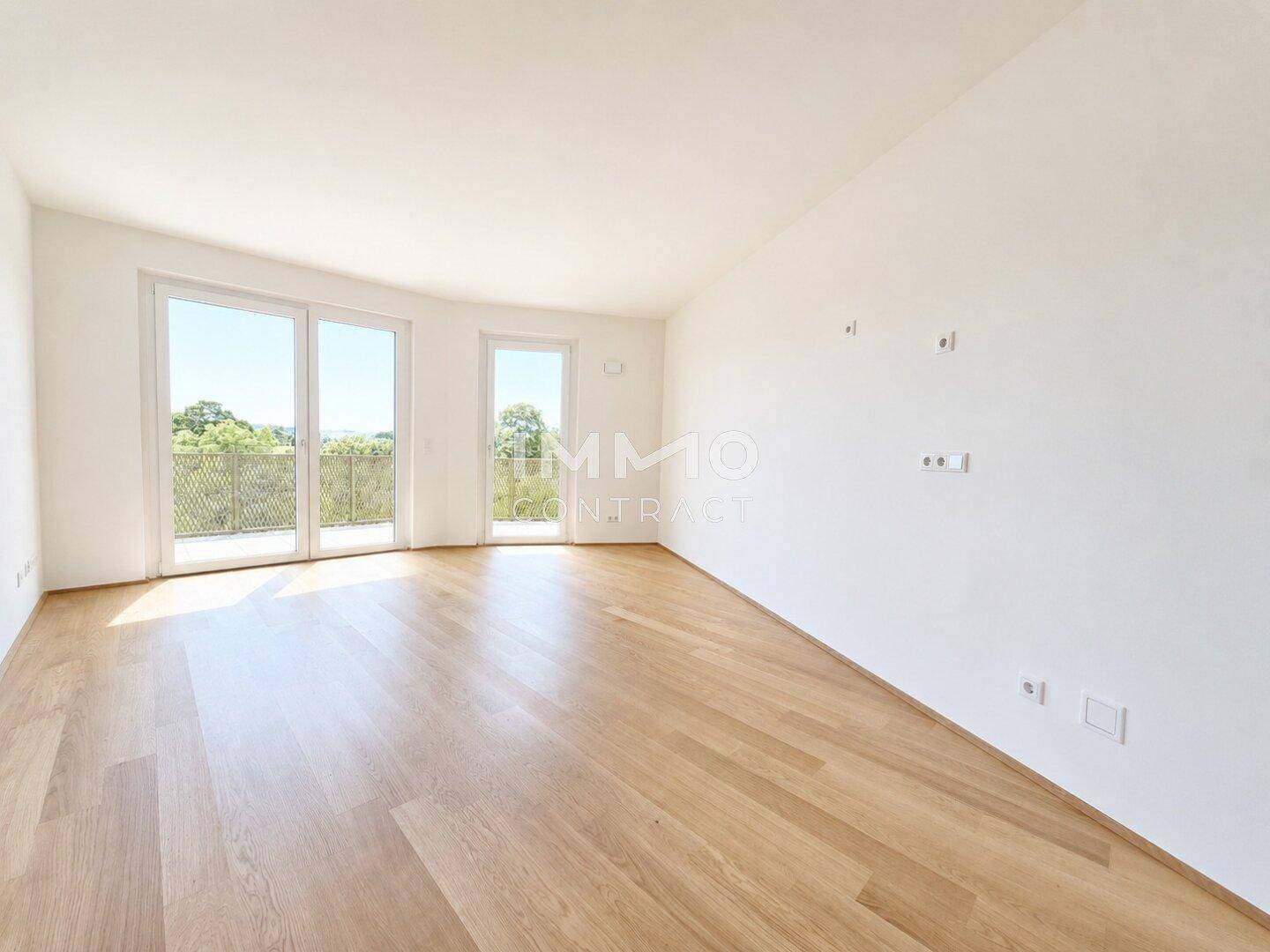 Heller Wohnraum mit Parkettboden, großen Fenstern und Zugang zu einem Balkon.