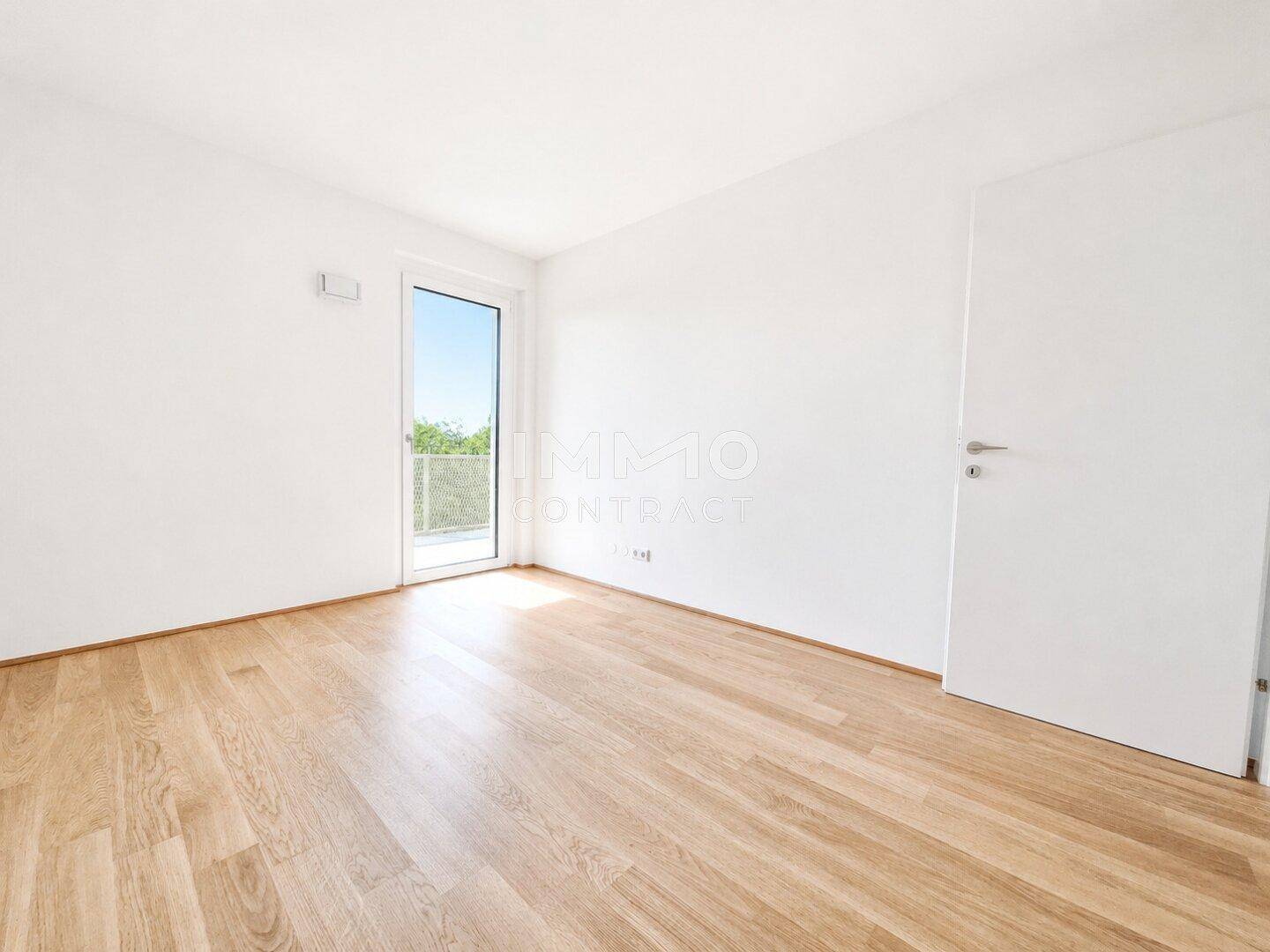 Helles Zimmer mit Parkettboden und einer Tür, die ins Freie führt.