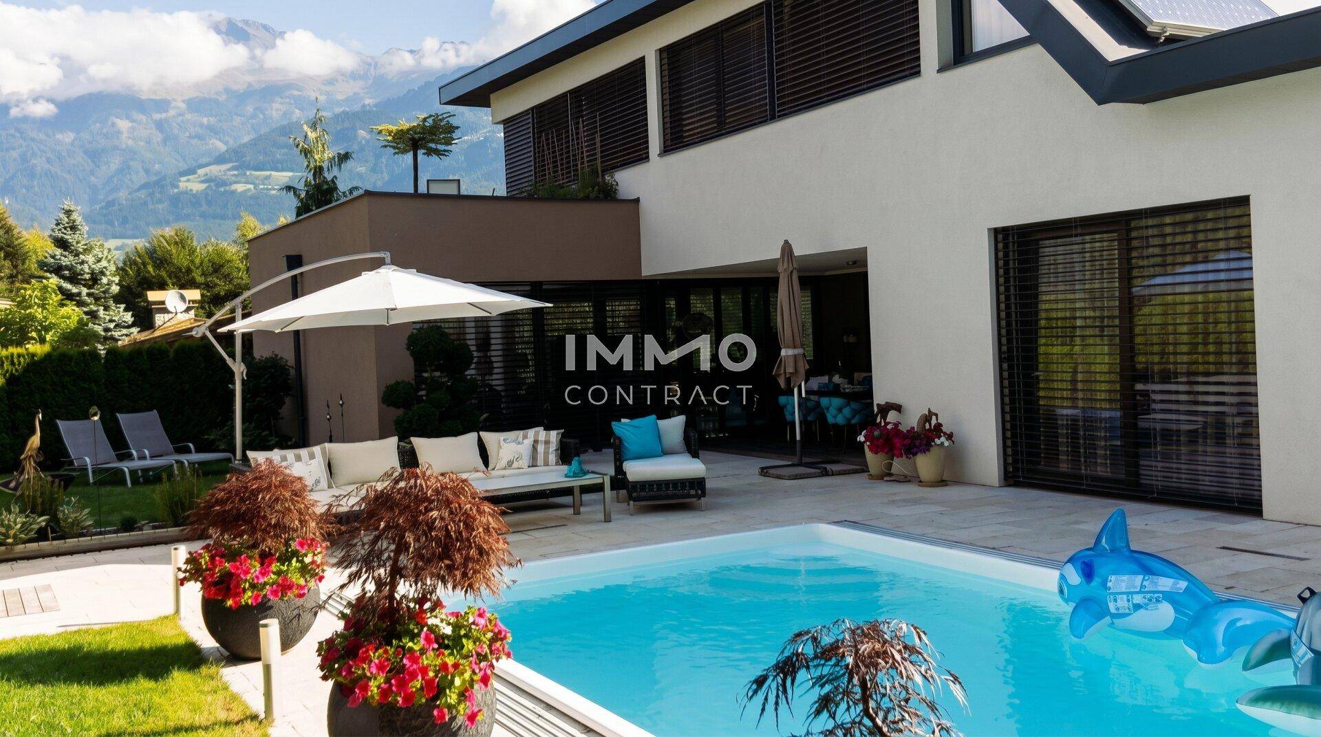 Moderner Außenbereich mit Pool, gemütlicher Sitzecke, gepflegtem Rasen und beeindruckendem Bergblick.