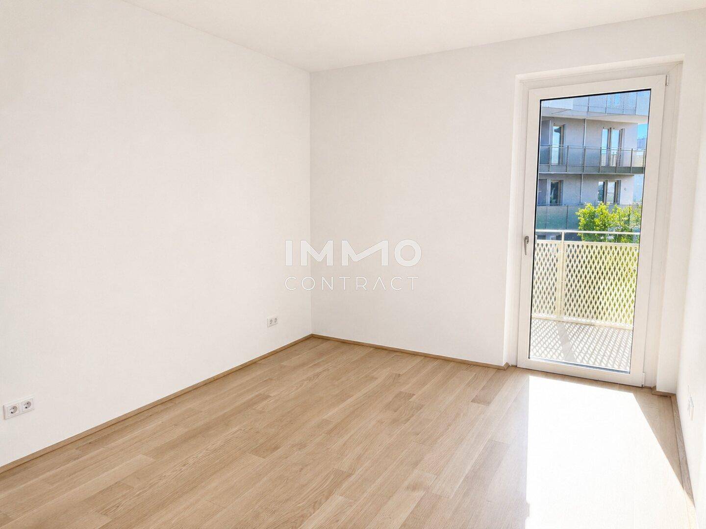 Unmöbliertes Schlafzimmer mit hellem Parkettboden und Zugang zu einem kleinen Balkon.