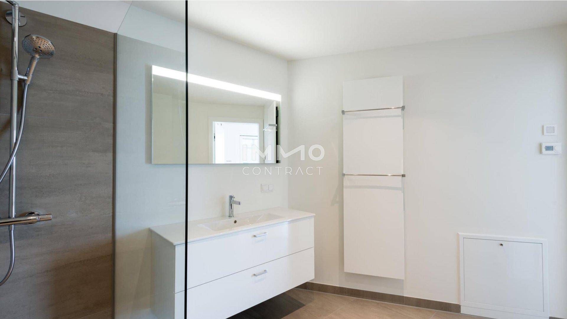 Modernes Badezimmer mit ebenerdiger Dusche, beleuchtetem Spiegel und beheiztem Handtuchhalter.