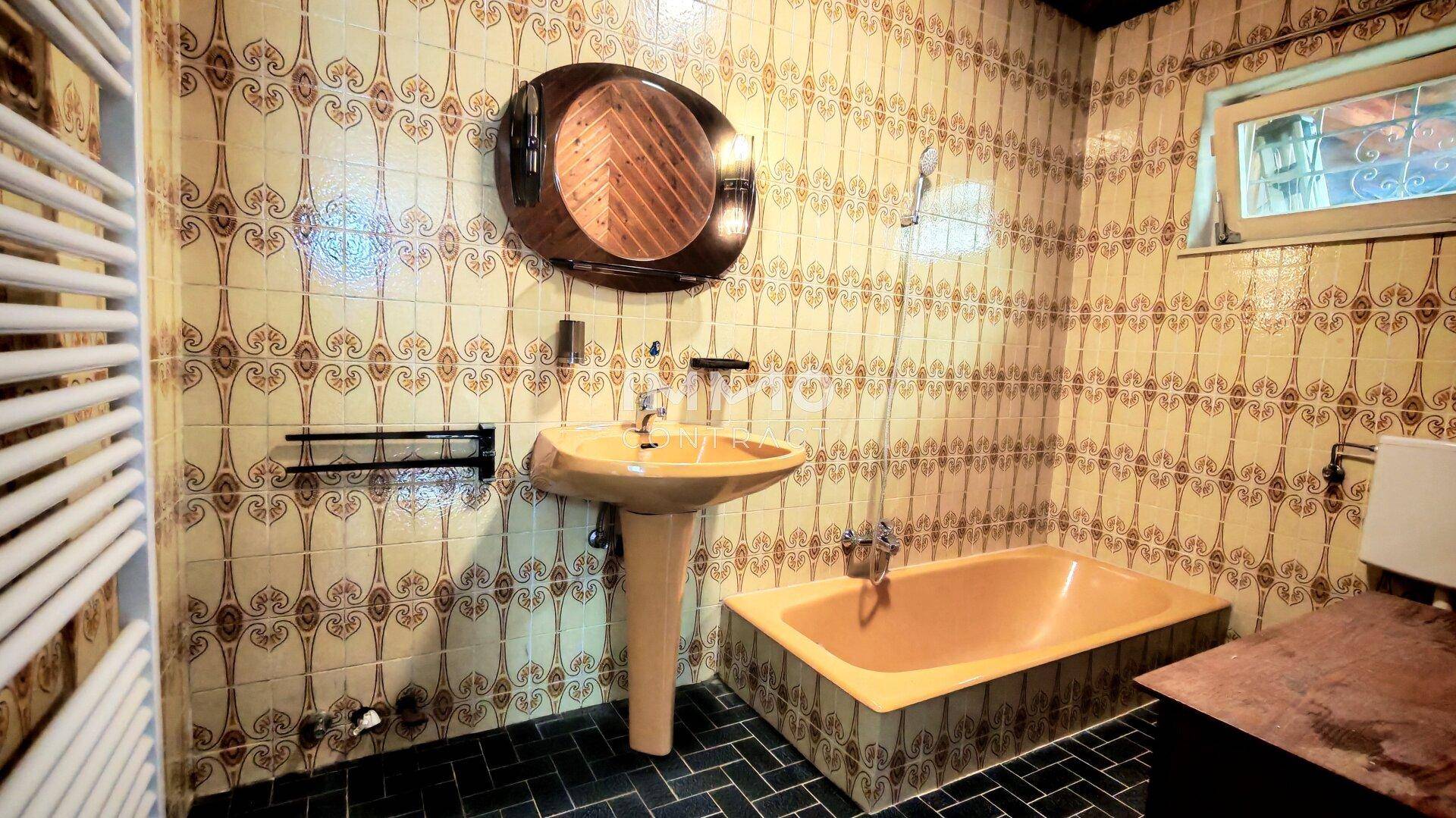 Badezimmer im Stil der 80er Jahre mit gelber Badewanne und gemusterten Fliesen.