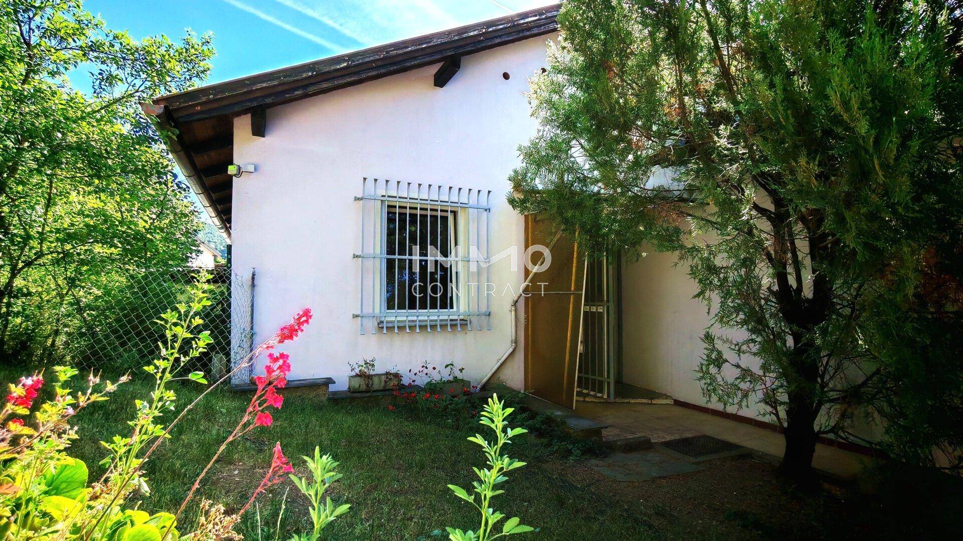 Seitenansicht des Hauses mit Fenstergittern und blühenden Pflanzen im Vorgarten.