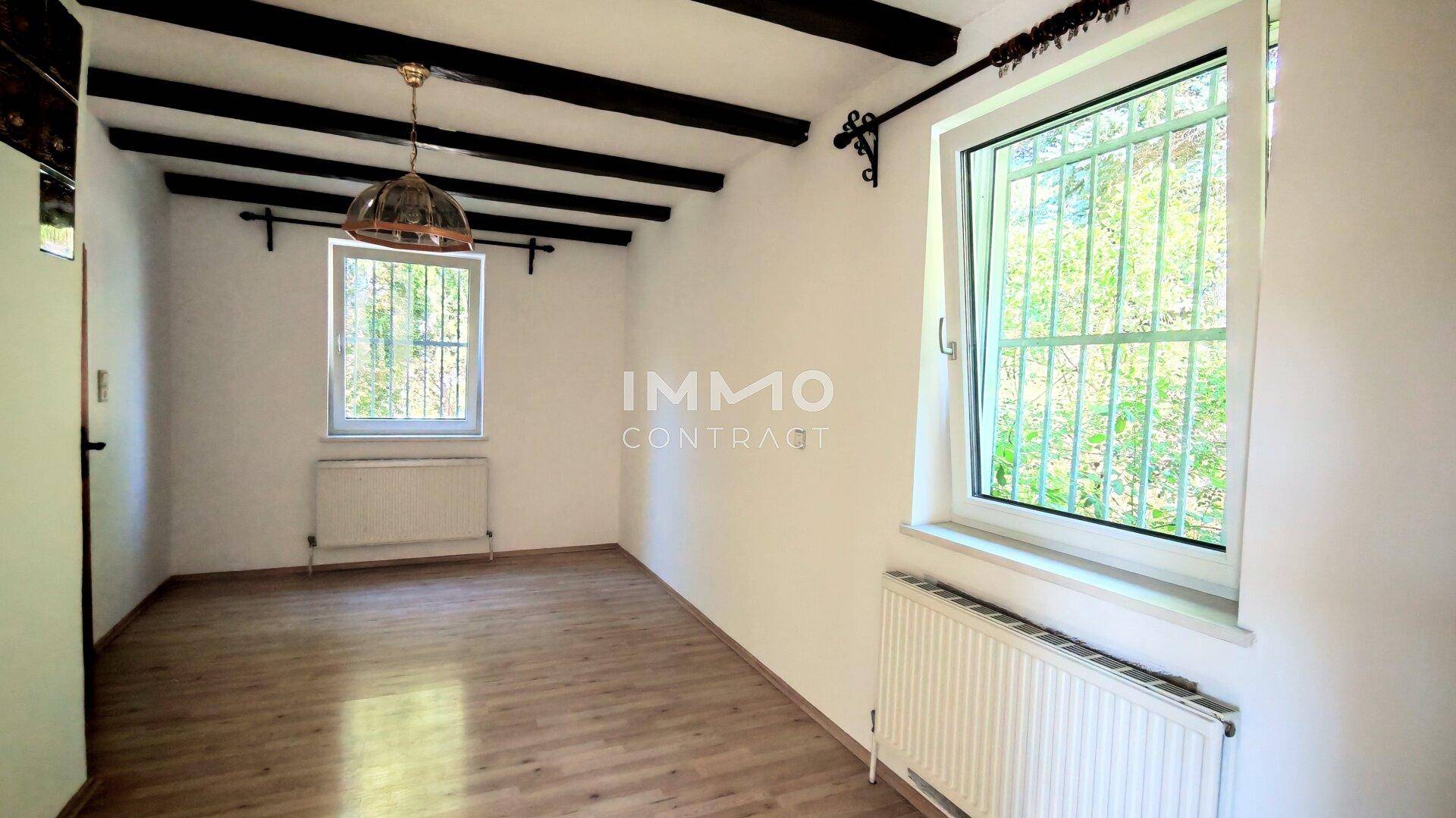 Gemütliches Zimmer mit Holzbalkendecke, Parkettboden und Fenster mit Gitter.