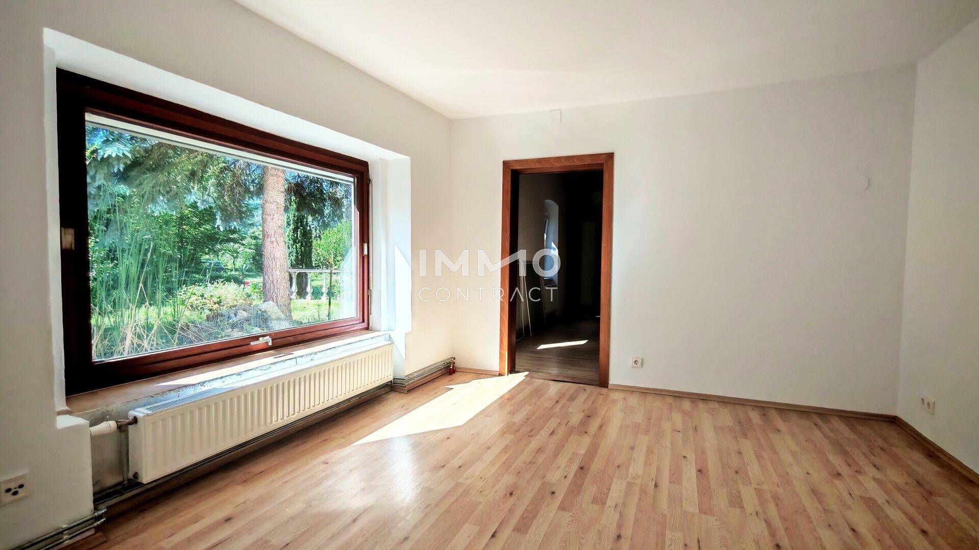 Helles Zimmer mit großem Fenster, Parkettboden und Blick ins Grüne.