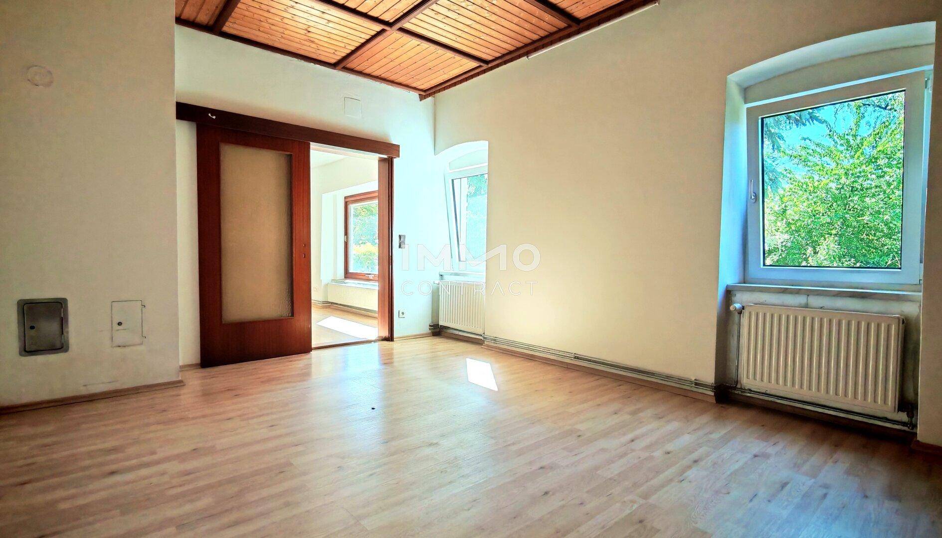 Geräumiges Zimmer mit Holzbalkendecke, Parkettboden und Schiebetür.