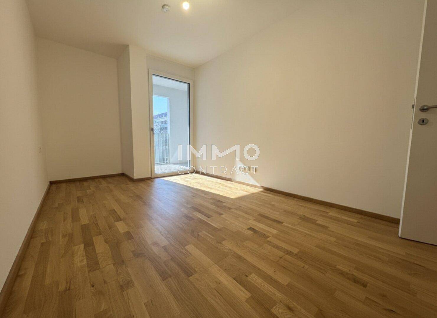 Helles, leeres Schlafzimmer mit Parkettboden und Zugang zu einem Außenbereich.