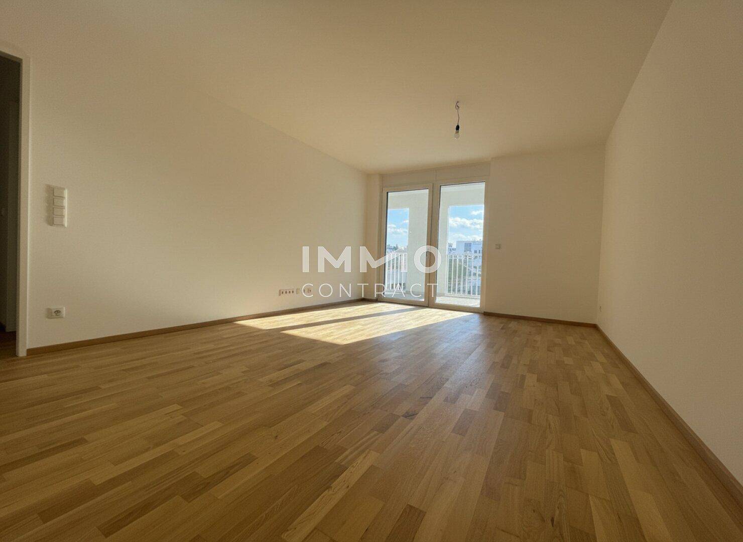 Geräumiges, leeres Wohnzimmer mit hellem Parkettboden und direktem Balkonzugang.