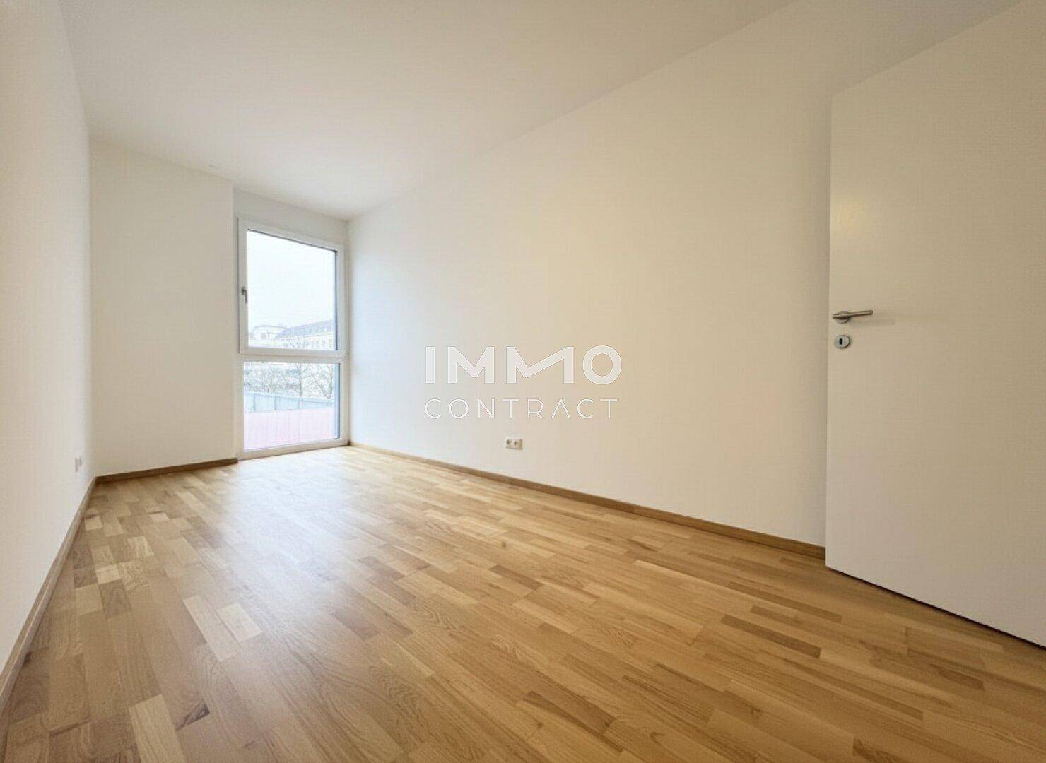 Heller, leerer Raum mit Parkettboden und großem Fenster, vielseitig nutzbar.