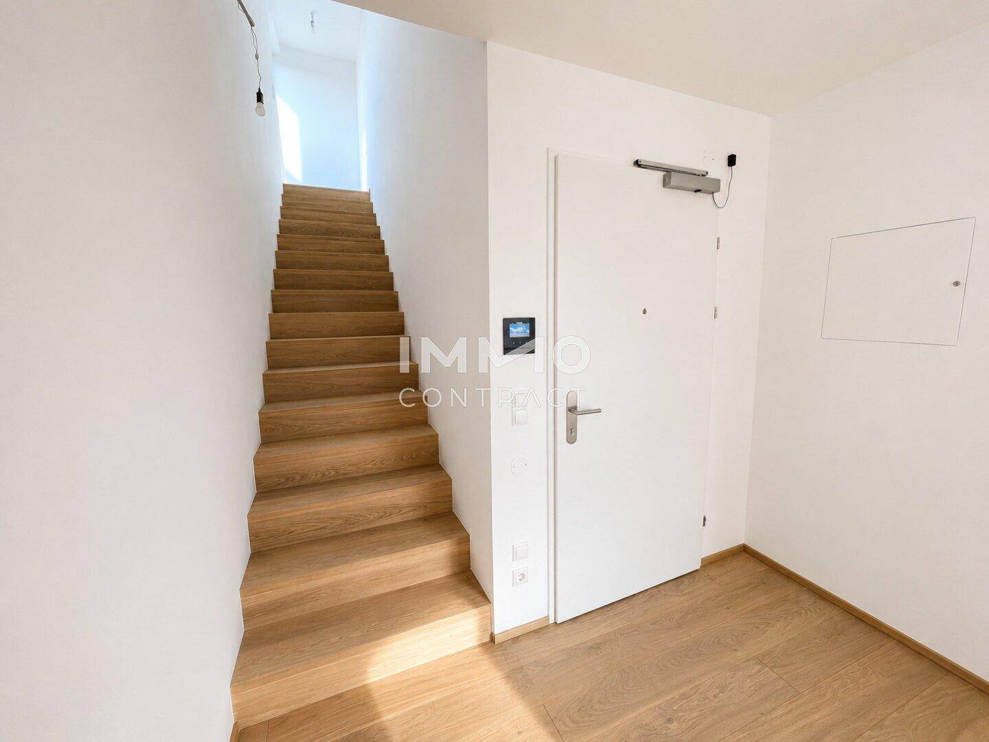 Eingangsbereich mit einer eleganten Holztreppe, die in die oberen Etagen führt, in hellem Design.